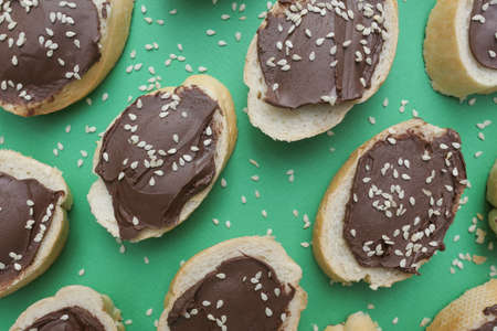 A lot of slices of white bread smeared with delicious chocolate paste, on a green background.