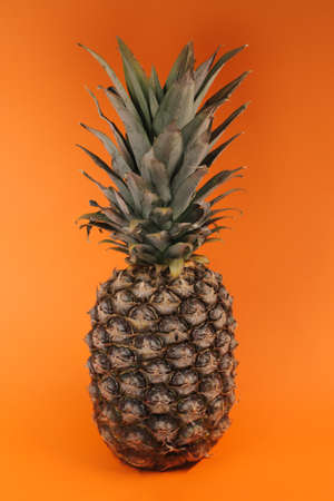 Large, ripe pineapple on an orange background full screen.