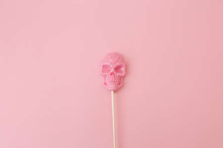 Sweetness on a stick, in the form of a pink skull on a colored background.の写真素材