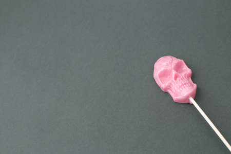 Sweetness on a stick, in the form of a pink skull on a colored background.の写真素材