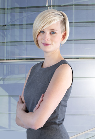 Young woman with crossed arms stands in front of a glass facade and smilesの写真素材