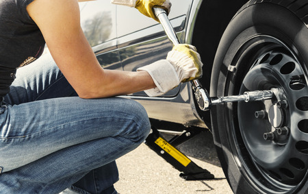 Woman is changing  tire of her car with wheel wrench の写真素材