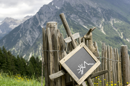 Wooden palisade with chalkboard hint panel in front of a mountain landscape  Chalkboard with empty space for own contentの写真素材