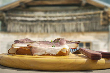 HDR image of cold cuts on wooden plate in front of a mountain hut in the alpsの写真素材
