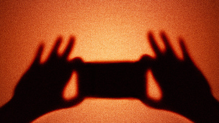 Shadow of smartphone photographer on spotlight illuminated grainy background