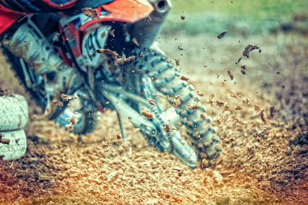 Rear view of drifting motocross bike. The rear wheel is digging deep in the mud and throws dirt in the air. Focus is on the throwing dirt nuggets. The motocross bike in the background is blurred.の写真素材