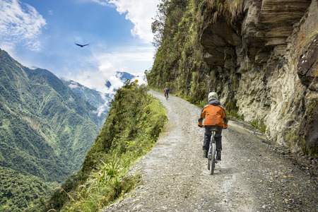 Bike adventure travel photo. Bike tourists  ride on the "road of death"  downhill track  in Bolivia. In the background sky circles a condor over the scene.の写真素材