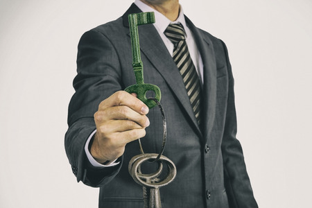 Man in business suit  holds a bunch of oversized historic keys in front of his body. The analogue film effect underlines the age of the keys.  The held and shown key has a green overlay. The photography can be used to illustrate environment themes.の写真素材