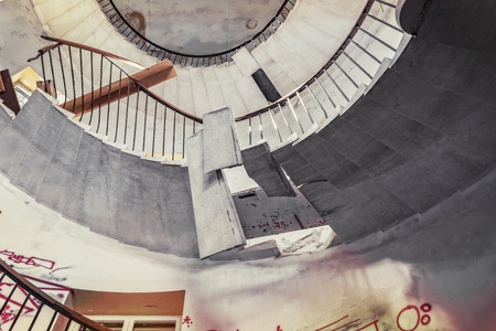 Bottom to top perspective of a desolate corkscrew staircase in an abandoned hotel ruin.