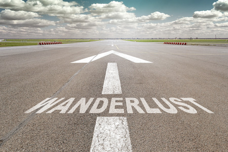 Runway of airport with arrow guideline and wanderlust  letters painted on the surfaceの写真素材