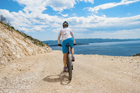 Rear view of woman biking bright gravel coast road in Croatia.の写真素材