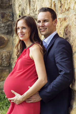 Stylish couple in the thirties with pregnant woman standing on medieval wall. They look into the distance.の写真素材
