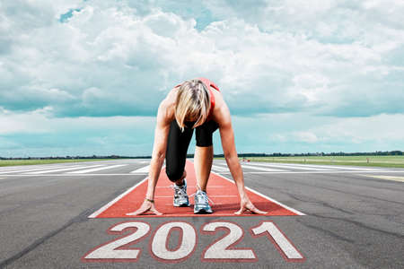 Female runner waits for her start at an airport runway. In the foreground the painted date 2021 symbolizes the year.の写真素材