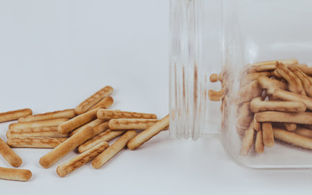Biscuit sticks in a glass jar on a white background.