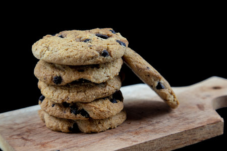 Chocolate chip cookies on a wooden plate with a black background.