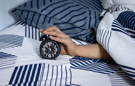 Deadline and Time management concept. Man hands holding Black alarm clock on bed. time to wake up...