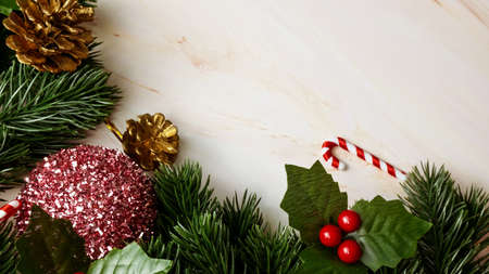 Green pine tree leaves, pink christmas decorations and candy canes on soft marble background,...