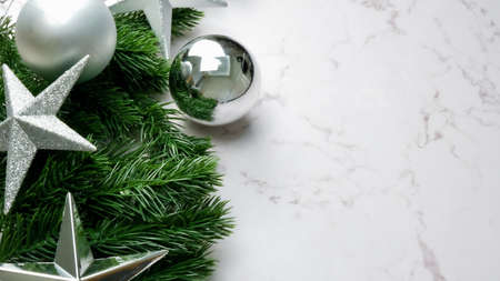 Green pine tree leaves on white marble background, christmas decorations in bright silver color. Simple and creative christmas concept.の写真素材