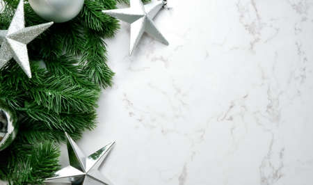 Green pine tree leaves on white marble background, christmas decorations in bright silver color. Simple and creative christmas concept.の写真素材