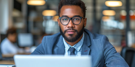 A man wearing glasses is seen sitting in front of a laptop, engrossed in his work.の素材
