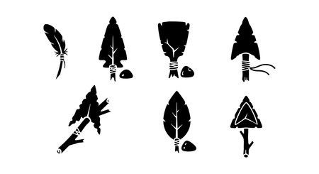 This vector features primitive stone arrowheads and feathers in black silhouette style, representing ancient hunting tools and tribal artifacts, evoking a vintage and mysterious atmosphere.のイラスト素材