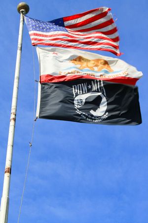 American California and POW flags over blue sky next to a veterans memorial.
