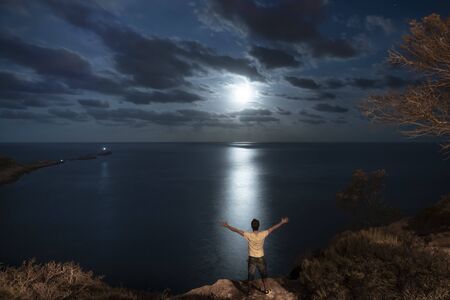 Cloudy nocturnal landscape at full moona. A man with open arms in a freedom and motivational...