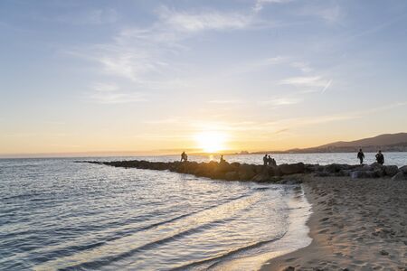 Palma de Mallorca, Balearics Islands, Spain - December 28, 2019:  Can Pere Antoni beach, in the city promenade, a stone pier with people watching the sunset in the skyline.のeditorial素材