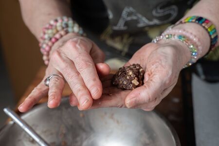Hands of older housewife woman in the kitchen, shaping the dough for oatmeal  and cocoa cookies, which is in a pastry bowlの写真素材