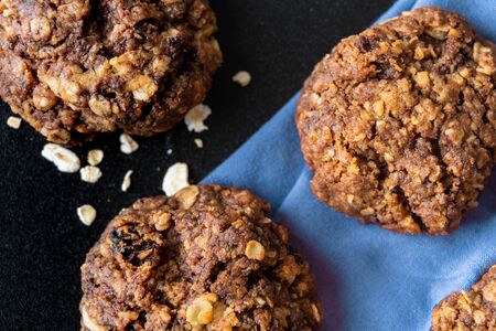Craft and rustic four oatmeal and cocoa cookies on a blue napkin, close up view. Dark food aesthetics, black background with several oat flakes.の写真素材