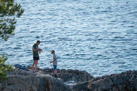 Calvia, Majorca, Spain - June 1, 2020: Two young brother fishermen in a cove placing the bait on the fishing rod, to start the fishing dayのeditorial素材
