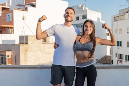 Young couple of athletes posing together and smiling, during a fitness session on their terraceの写真素材