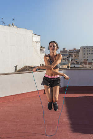 Young woman skipping rope and doing physical training on the terrace of the building, in an urban settingの写真素材