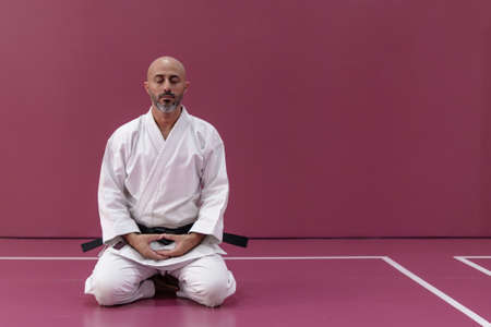 Karate master sitting in meditation pose, back turned, in his dojo or martial arts school