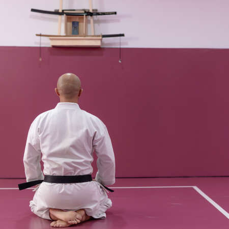 Karate master sitting in meditation pose, back turned, in his dojo or martial arts school