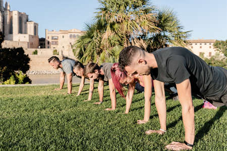 Group of sporty friends doing squat exercise and having fun at outdoor fitness session in city parkの写真素材