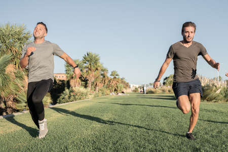 Two young sporty boys competing in a running race, on the grass of the parkの写真素材