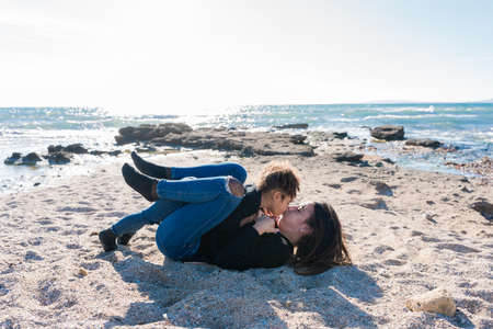 Affectionate kiss between a young mother and her African American daughter, in the sand on the beachの写真素材