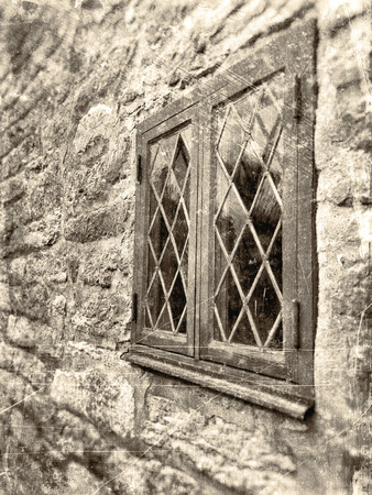 Window in angle with leaded windowpane surrounded by a rough stone wall, textured in sepia with scratches and stains.の写真素材