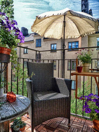 Artistic textured image of cosy decorated city balcony in summertime, with chair and parasol on wooden floor.の写真素材
