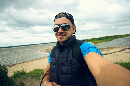 Man takes pictures of himself on the background of the river