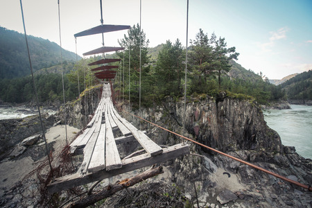 Abandoned suspended pedestrian bridge in mountainsの写真素材