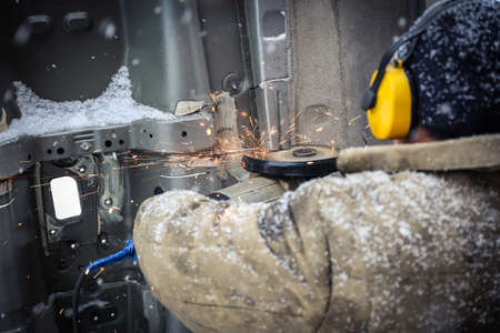 Worker in dirty clothes saws metal in winter in snowfallの写真素材