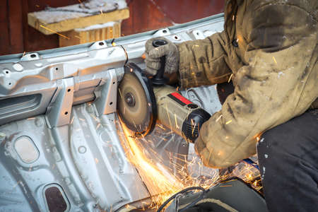 Worker in dirty clothes saws metal in winter in snowfallの写真素材