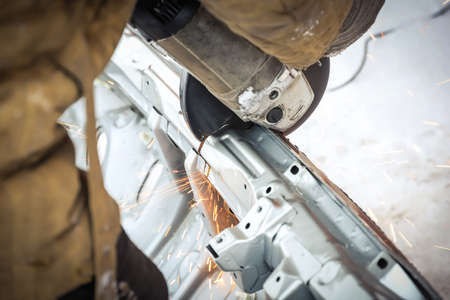 Worker in dirty clothes saws metal in winter in snowfallの写真素材