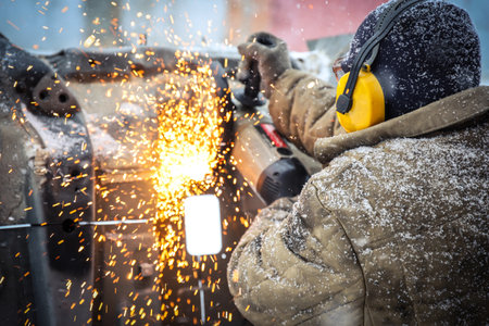 Worker in dirty clothes saws metal in winter in snowfallの写真素材