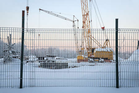 Construction behind a fence in cold winter against the background of frozen treesの写真素材