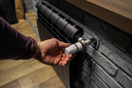 The valve of a home black radiator adjusting the temperature in the room. Hand adjustmenの写真素材