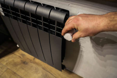The valve of a home black radiator adjusting the temperature in the room. Hand adjustmenの写真素材