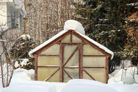 Snow covered greenhouse in the vegetable garden in winter close-up. Outdoorsの写真素材
